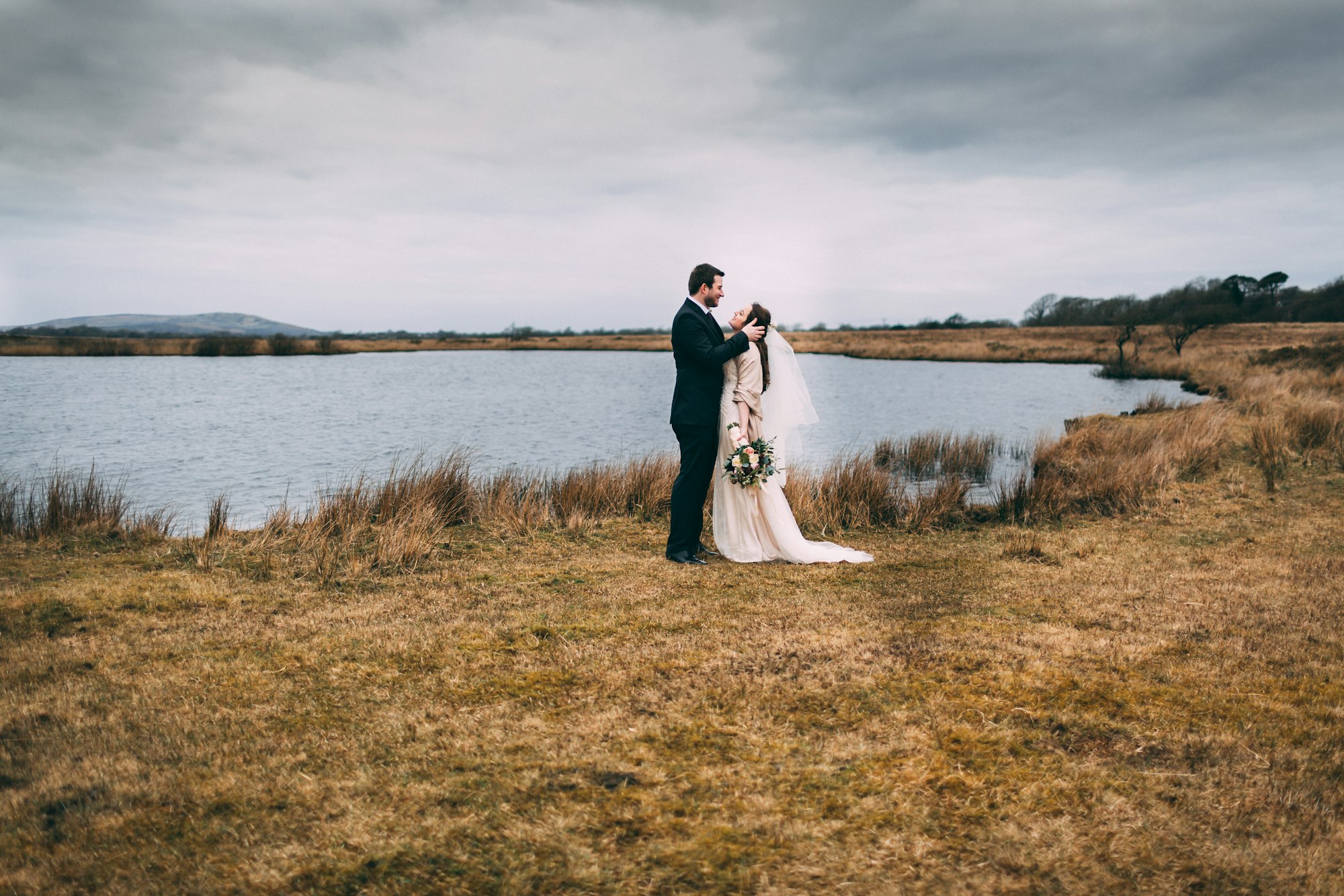 A couple on a hillside beside a lake on their wedding day